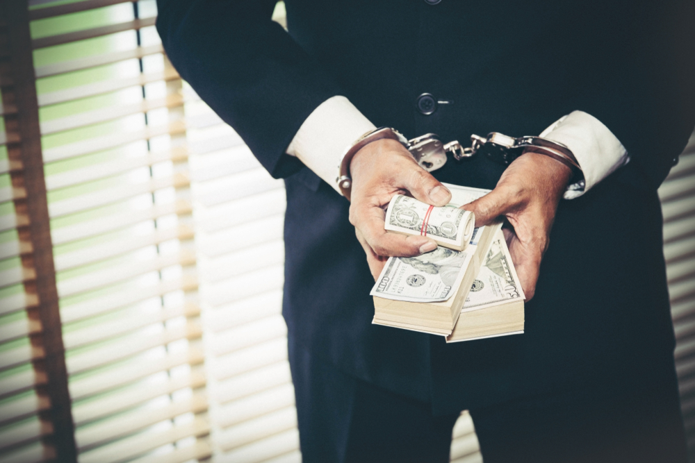 man in suit handcuffed and holding dollar notes