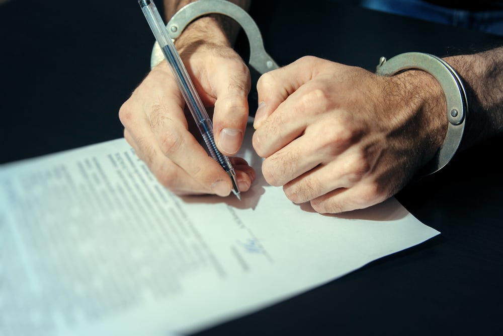 handcuffed person signing a guilty plea agreement